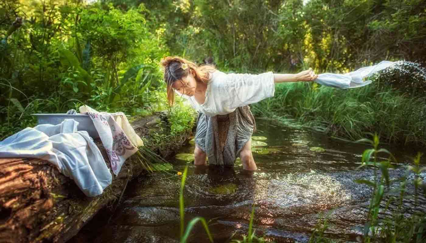 Женщина стирает бельё в водоеме и купается спасаясь от жары
